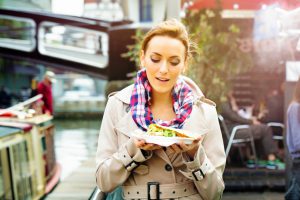 Young British woman looks at take-out food with appetite as she walks out in London, UK on a late Autumn afternoon. She is dressed in warm clothing and a warm light bathes the image.